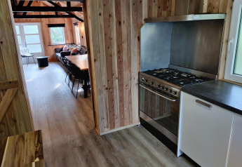 Küche mit Holzverkleidung und Blick ins Wohnzimmer in der Glamping-Unterkunft Groupaccommodation 'de Blokhut'.