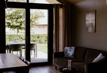 Innenaufnahme einer gemütlichen Lodge mit großen Fenstern, Sofa und Esstisch im Holiday Park Eigen Wijze.