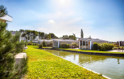 Solrig udsigt over lodges ved Resort Mooi Bemelen i Nederlandene, omgivet af kanal og grønne områder.