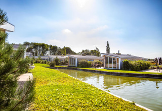 Vista soleada de cabañas en Resort Mooi Bemelen, Países Bajos, junto a un canal y áreas verdes ajardinadas.