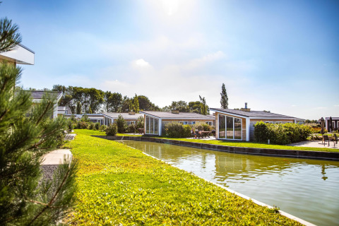 Sunny view of lodges at Resort Mooi Bemelen in the Netherlands, with a canal and green landscaped surroundings.