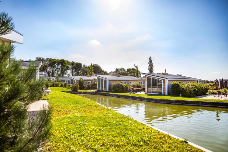 Sunny view of lodges at Resort Mooi Bemelen in the Netherlands, with a canal and green landscaped surroundings.