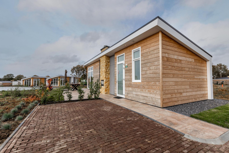 Modern wooden lodge at Resort Mooi Bemelen in the Netherlands, featuring brick paving and garden landscaping.