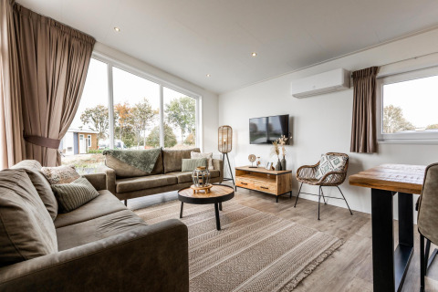 Sala de estar moderna en una cabaña Biebosch del Resort Mooi Bemelen en los Países Bajos, con gran ventanal.