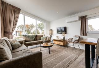 Moderne woonkamer in een Biebosch lodge op Resort Mooi Bemelen in Nederland met grote ramen en sfeervolle inrichting.