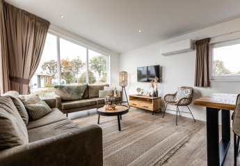 Moderne stue i en lodge på Resort Mooi Bemelen i Holland med store vinduer og komfortable sofaer.