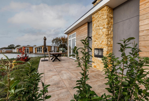 Terraza exterior en Lodge Biebosch, Resort Mooi Bemelen, Países Bajos, con vista al lago y casas modernas.