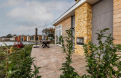 Patio at Lodge Biebosch, Resort Mooi Bemelen, Netherlands, with stone wall, plants, and modern lakeside lodges.