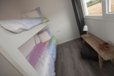 Room with bunk beds, wooden table, lamp, and window in the Biebosch lodge at Resort Mooi Bemelen, Netherlands.