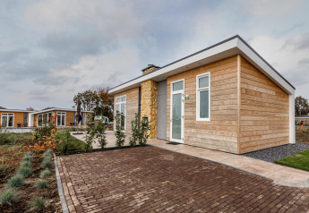 Modern wooden lodge at Resort Mooi Bemelen in the Netherlands, featuring a garden and brick-paved entrance.