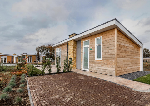 Modern wooden lodge at Resort Mooi Bemelen in the Netherlands, featuring a garden and brick-paved entrance.