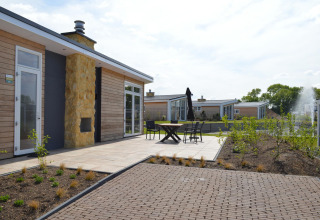 Terraza exterior de la moderna cabaña Biebosch en Resort Mooi Bemelen, Países Bajos, con mesas y sillas.
