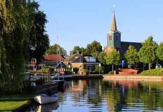 Foto einer idyllischen Glamping-Unterkunft am Wasser mit Booten, Kirche und grüner Landschaft.