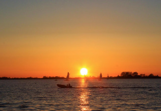 Atardecer sobre el lago con veleros y una lancha motora desde un alojamiento glamping, ambiente tranquilo.