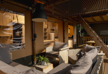 Zona de descanso exterior en una tienda safari en Wilsumer Berge, Alemania, con muebles de madera y cojines.