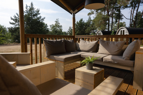 Zona de descanso exterior en una tienda safari en Wilsumer Berge, Alemania, con muebles de madera y cojines.