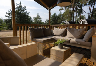 Zona de descanso exterior en una tienda safari en Wilsumer Berge, Alemania, con muebles de madera y cojines.