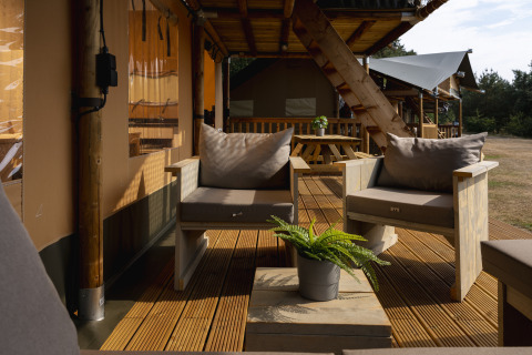 Zona de estar exterior en la tienda Safari de Wilsumer Berge, Alemania, con muebles de madera y plantas.