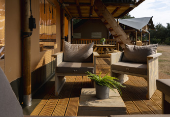 Zona de estar exterior en la tienda Safari de Wilsumer Berge, Alemania, con muebles de madera y plantas.