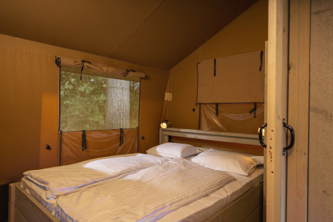 Vista interior de una tienda safari con cama doble y ventana al bosque en Wilsumer Berge, Alemania.