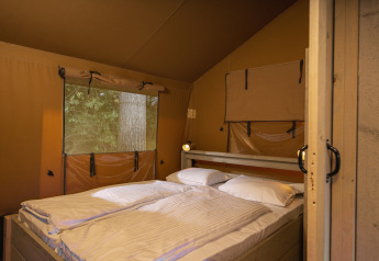 Vista interior de una tienda safari con cama doble y ventana al bosque en Wilsumer Berge, Alemania.