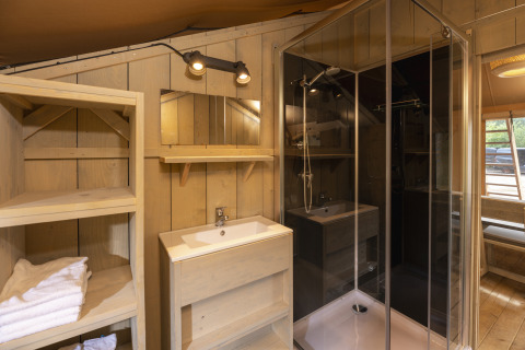Baño dentro de la tienda Safari en Wilsumer Berge, Alemania, con ducha, lavabo, estantería y paredes de madera.