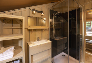 Baño dentro de la tienda Safari en Wilsumer Berge, Alemania, con ducha, lavabo, estantería y paredes de madera.