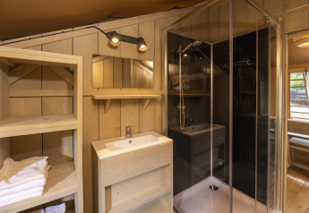 Baño dentro de la tienda Safari en Wilsumer Berge, Alemania, con ducha, lavabo, estantería y paredes de madera.