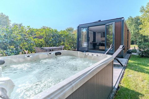 Whirlpool und Liegestühle vor einer modernen Waldhütte im Holiday Park BreeBronne, Niederlande.