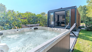 Whirlpool und Liegestühle vor einer modernen Waldhütte im Holiday Park BreeBronne, Niederlande.
