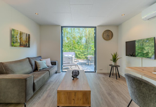Modernes Wohnzimmer in einer Forest Cabin im Holiday Park BreeBronne, Niederlande, mit Blick ins Grüne.