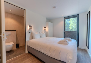 Chambre moderne avec lit double, salle de bain attenante et grande fenêtre à Forest Cabin, BreeBronne, Pays-Bas.