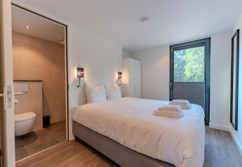 Chambre moderne avec lit double, salle de bain attenante et grande fenêtre à Forest Cabin, BreeBronne, Pays-Bas.