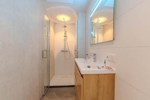 Baño moderno con ducha de vidrio, tocador de madera y espejo LED en Forest Cabin, Holiday Park BreeBronne.