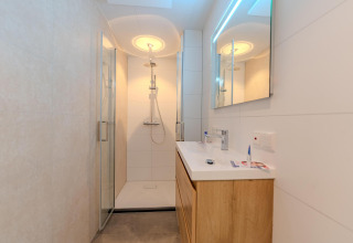 Baño moderno con ducha de vidrio, tocador de madera y espejo LED en Forest Cabin, Holiday Park BreeBronne.
