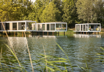 Würfelförmige Lodges am Wasser auf Stelzen, umgeben von Bäumen und ruhiger Naturumgebung.