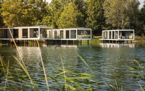 Water Cube-lodges op palen boven een rustig meer, omringd door groen en natuurlijke omgeving.