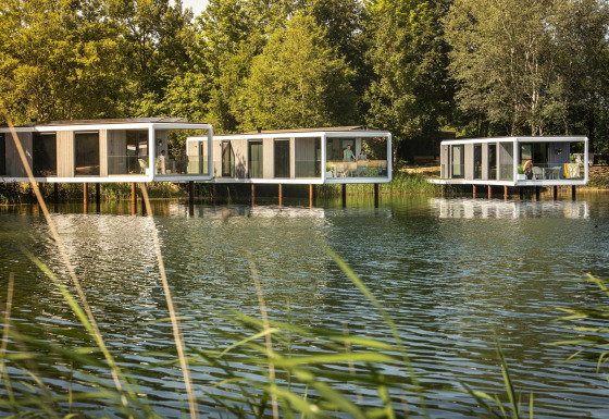Water Cube-lodges op palen boven een rustig meer, omringd door groen en natuurlijke omgeving.