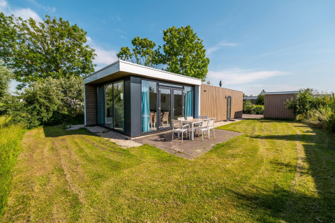 Lodge tipo pabellón moderno con ventanales grandes, comedor exterior y césped en Poort van Zeeland, Países Bajos.