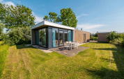 Lodge tipo pabellón moderno con ventanales grandes, comedor exterior y césped en Poort van Zeeland, Países Bajos.