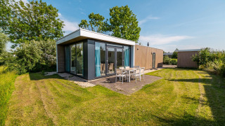 Modern pavilion lodge with large windows and outdoor dining set in a green yard at Poort van Zeeland, Netherlands.