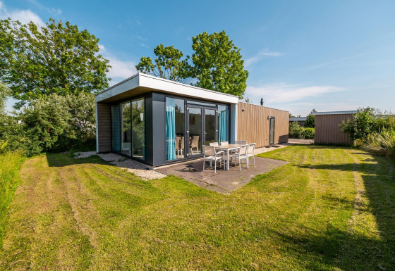 Lodge tipo pabellón moderno con ventanales grandes, comedor exterior y césped en Poort van Zeeland, Países Bajos.