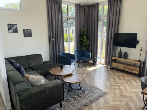 Sala moderna en el lodge Pavilion en Poort van Zeeland, Países Bajos, con sofá, sillones y grandes ventanas.