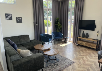 Sala moderna en el lodge Pavilion en Poort van Zeeland, Países Bajos, con sofá, sillones y grandes ventanas.