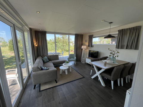 Lichte, moderne paviljoenwoonkamer met grote ramen, eettafel en bank bij Poort van Zeeland, Nederland.