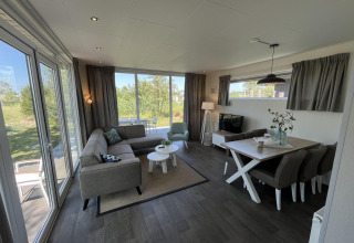 Salon lumineux et moderne de pavillon avec grandes fenêtres, salle à manger et canapé à Poort van Zeeland, Pays-Bas.