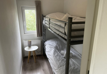 Pequeño dormitorio con litera, ventana, mesa auxiliar y lámpara en Pavilion at Poort van Zeeland, Países Bajos.