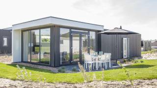 Moderne lodge Pavilion bij Poort van Zeeland, Nederland, met grote ramen en buitenterras met tafel.