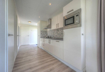 Moderne køkkenindretning med hvide skabe, trægulv og mosaikfliser på Pavilion ved Poort van Zeeland.