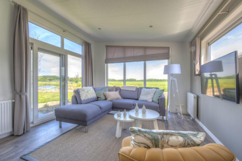 Helles, modernes Wohnzimmer in einer Lodge des Pavilion Poort van Zeeland, mit großen Fenstern und Blick ins Grüne.